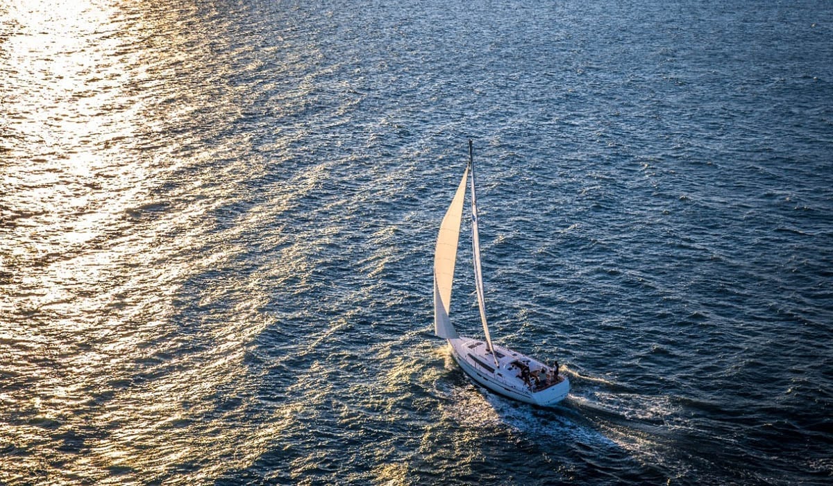 Un voilier naviguant au milieu de l'océan avec le reflet du soleil sur l'eau.